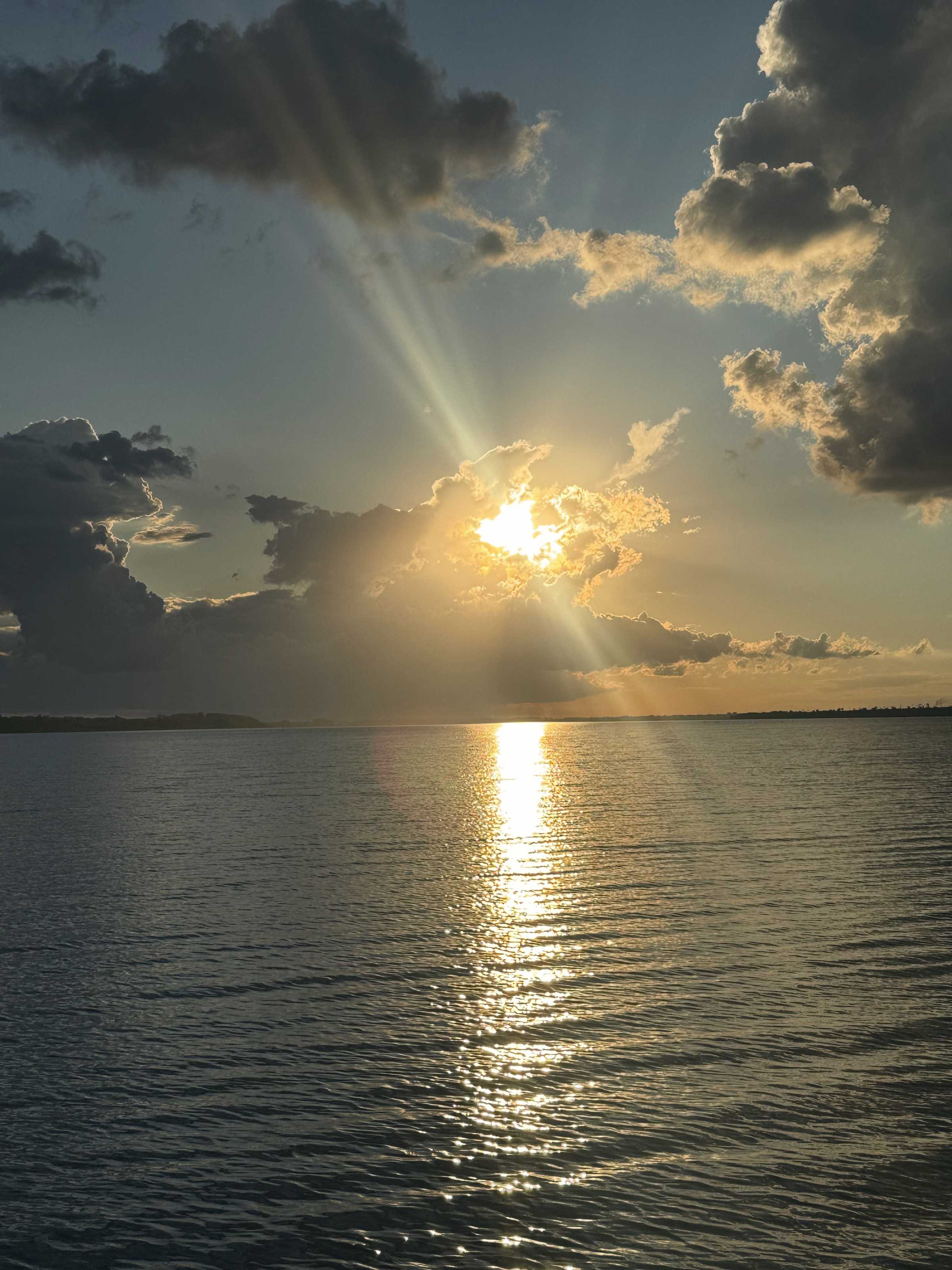The sun sets between clouds over the lake, leaving a golden reflection on the water.
