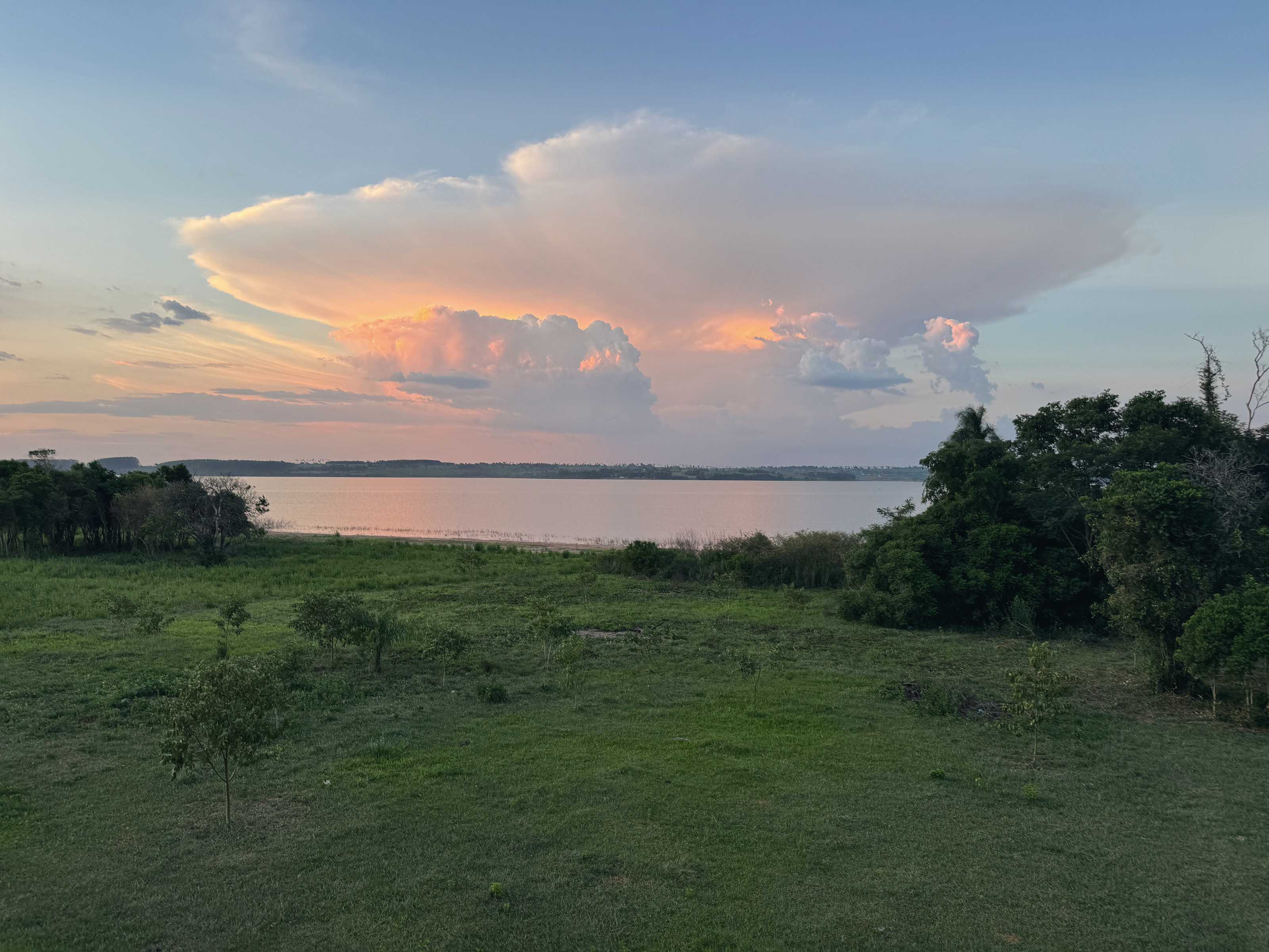 A towering cumulus cloud, pink with the sunset, above the still lake and the fields.