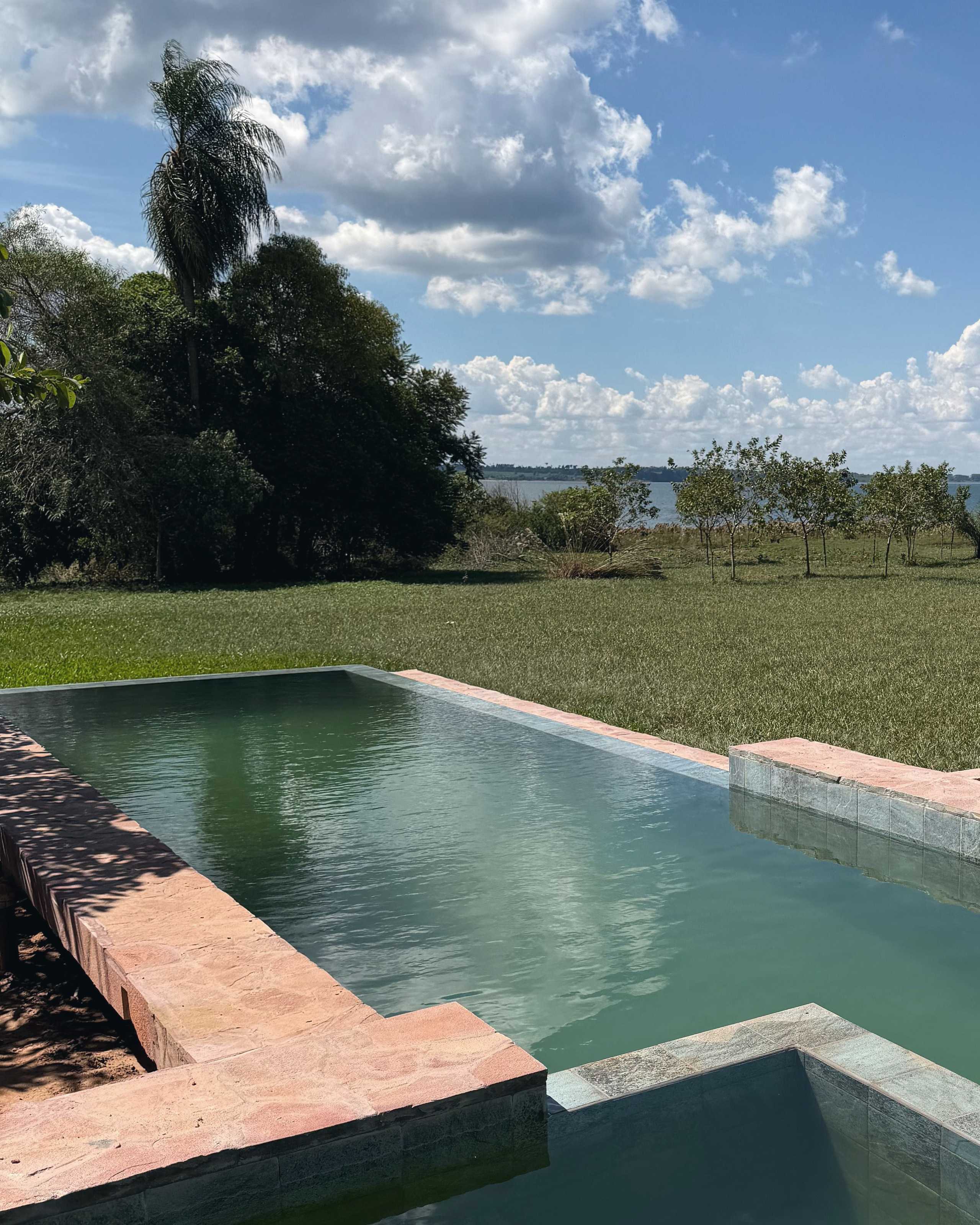 The green-water pool with its pink stone edge, and the lake between the trees beyond.